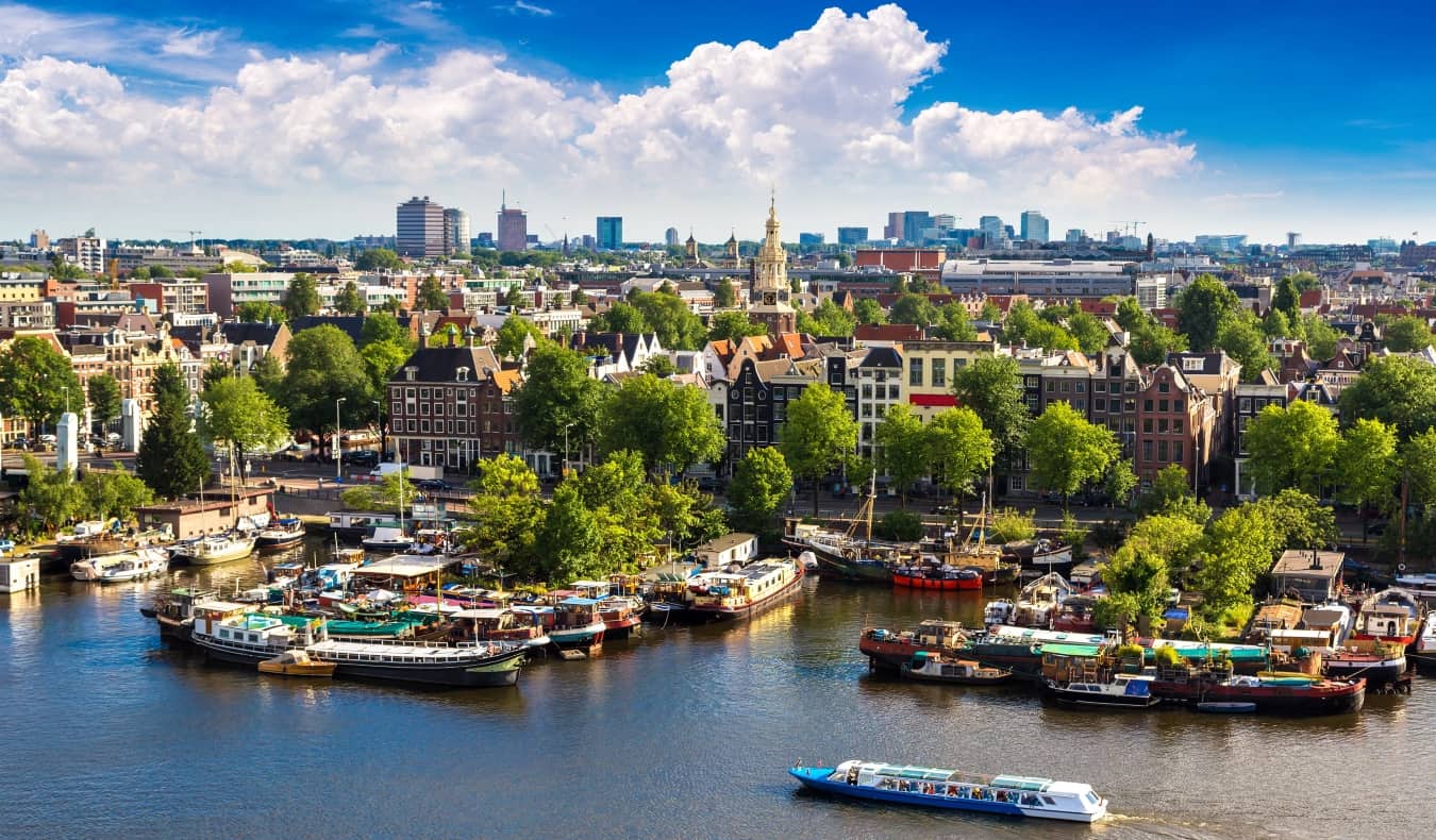 Panoramic view of the Amsterdam skyline with boats docked and floating along a river in the foreground