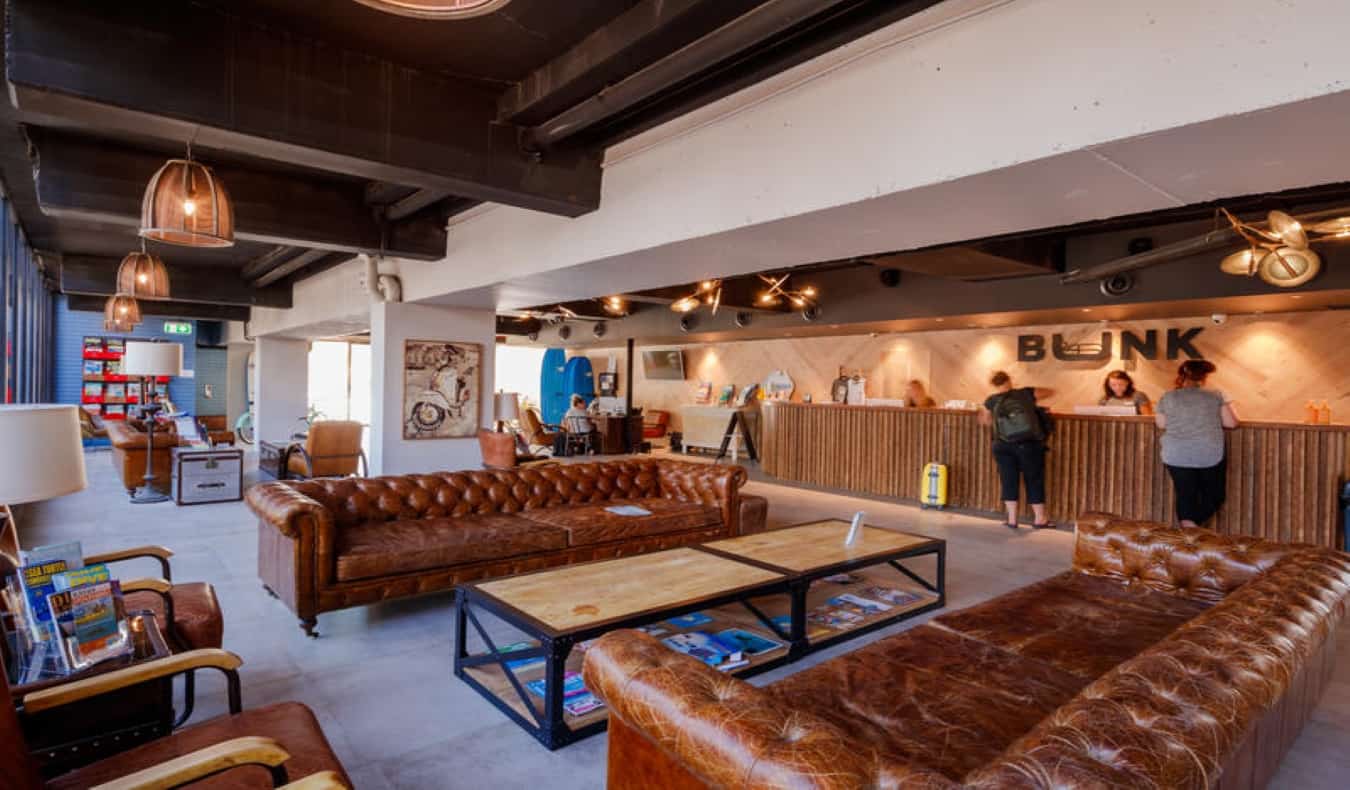 Common area with large leather couches and people checking in at long front desk at BUNK Surfers Paradise in Australia.