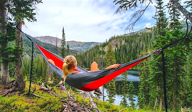 A woman sitting in a hammock overlooking a lake in the woods