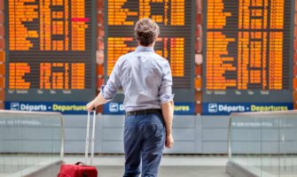 A man standing beside his luggage looking at an airport flight board