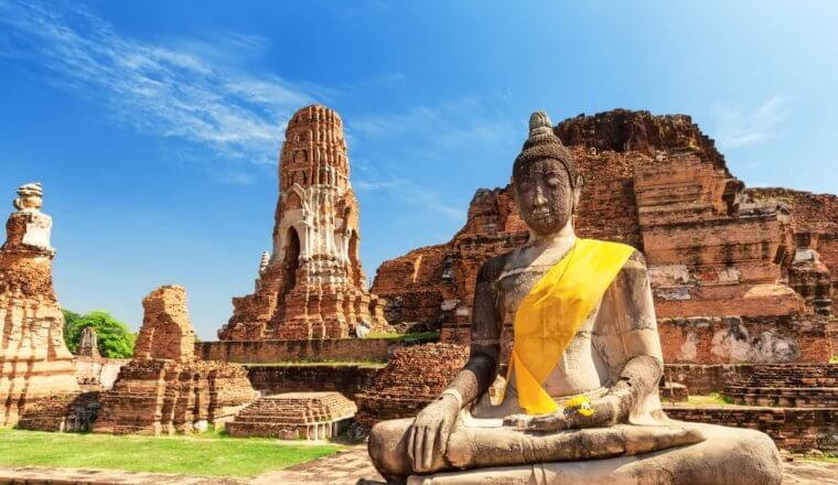 An ancient Buddha statue with a sash at a historic site in sunny Thailand