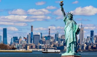 The iconic Statue of Liberty with NYC in the background on a sunny day with blue skies