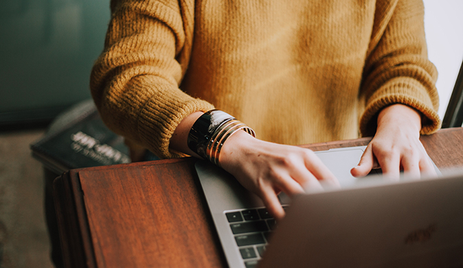 a woman in a yellow sweater writes from her laptop