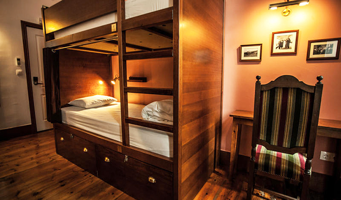 Dark wooden bunk beds and desk with chair in dorm room at Home Lisbon Hostel