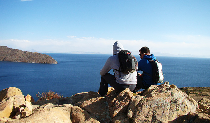 two travelers sitting on a rock near the ocean