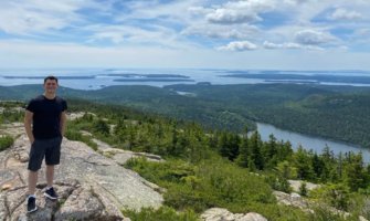 Matt standing on top of a mountain with a lush archipelago behind him in Maine, USA