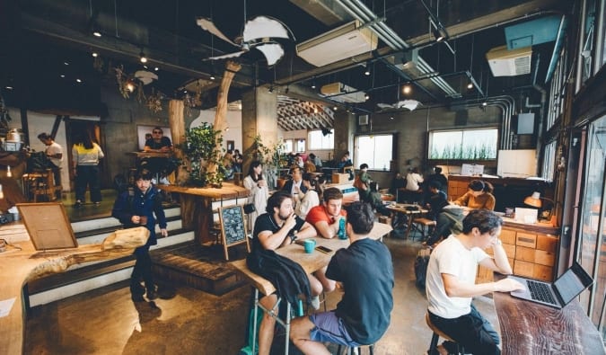 The bustling cafe space and common area with people in groups talking and others working on their laptops at Nui. hostel in Tokyo, Japan