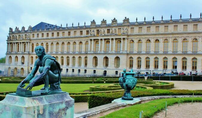 palace of versailles image taken from the gardens facing the palace in the foreground is a statue of a man crouching down and looking into the distance