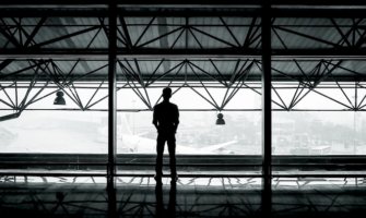 A man staring out of an airport window looking at airplanes