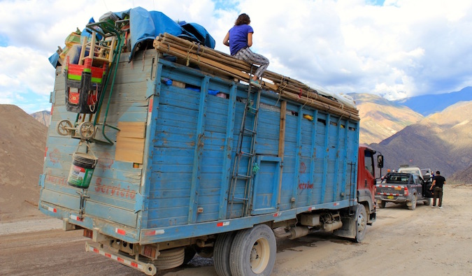 A backpacker hitchhiking on top of a truck in Peru