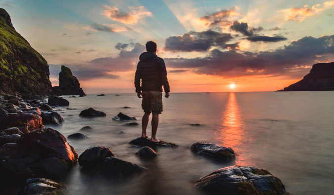 A solo traveler posing for a moody photo at sunset while standing on a beach