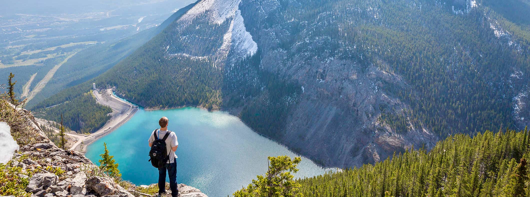 a solo hiker admiring the view over the mountains of Canada with a lake in the distance