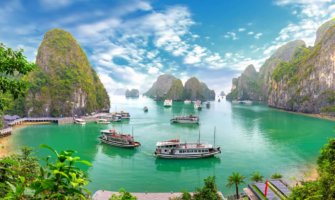 Boats in the calm waters of Ha Long Bay near Hanoi, Vietnam surrounded by tall mountains