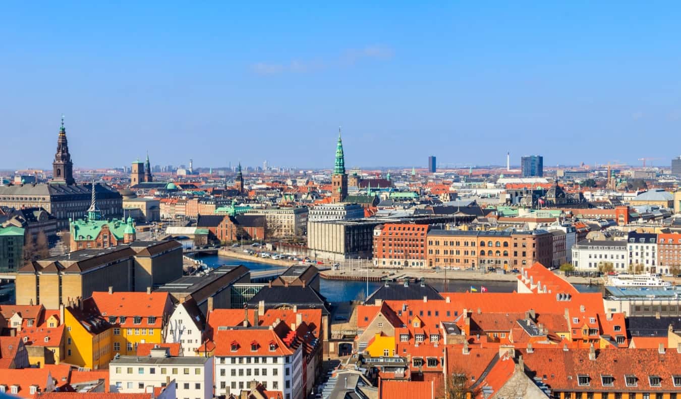 Aerial view of Copenhagen, Denmark, with red rooftops, a canal, and church steeples dotting the cityscape